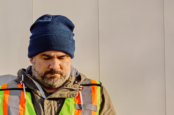 A man wearing a high visibility vest and warm clothes looks downwards